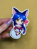 Sticker of a character with fox hair and cat ears held by a hand on a beige background