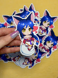 Anime-style character of Ahri from League of Legends sticker held by a hand with multiple stickers in the background on a yellow background