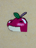 A sticker in the shape of an alligator head with the colors of an apple above a yellow background.