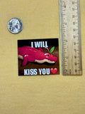Sticker with a pink creature and text 'I WILL KISS YOU' next to a ruler for size reference on a beige background.