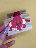 Hand holding a small sticker with a red creature illustration on a yellow background