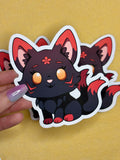 A hand holds a black and red kitsune with two tails over a yellow background.