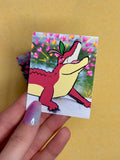 Hand holding a colorful sticker with a cartoon character on a yellow background