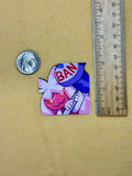 Small sticker with a character holding a 'BAN' sign next to a quarter and ruler on a beige background